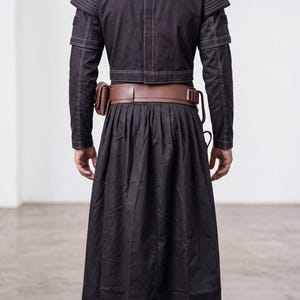 Op de afbeelding: Een volledig kostuum met een metallic zilveren helm, een zwart jasje met lange mouwen en witte contraststiksels, een bruine leren gereedschapsriem met tasjes, een lange zwarte geplooide rok, een zwarte broek en zwarte laarzen.