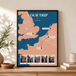 May include: A framed wall art print featuring a map of Europe with a peach-coloured landmass and dark blue ocean. The map displays a travel route connecting London, Amsterdam, Brussels, and Paris with red location pins and five photo frames.