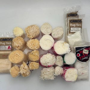 Puede incluir: Una colección de carretes de hilo para alfombras de color blanco y crema, algunos con la marca "CARON Rug Yarn" y "Easy Care Acrylic Fiber by Monsanto" impresa en la etiqueta. También hay un carrete de hilo con la marca "RED HEART" impresa en la etiqueta.