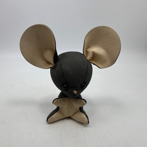 May include: A small, plush mouse toy with large, beige ears and a black, felt body. The mouse has black button eyes and a small, pink nose.
