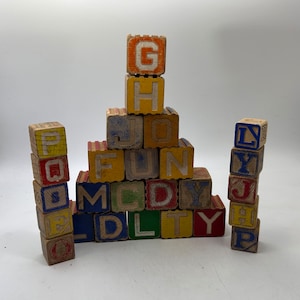 May include: A stack of wooden blocks with letters spelling out "G, H, J, O, FUN, M, C, D, L, T, Y" in a rainbow of colors. The blocks are arranged in a pyramid shape.