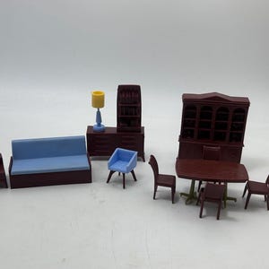 以下が含まれることがあります： ミニチュアのドールハウス家具のコレクション。ソファ、椅子、テーブル、ランプ、キャビネットなど。家具は主に濃い赤色で、青と黄色のアクセントが付いています。セットには、椅子とハッチを備えたダイニングテーブルが含まれています。