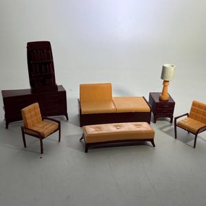 May include: A miniature dollhouse furniture set featuring a dark brown cabinet with a tall hutch, a two-tone sofa with a light orange seat, a matching light orange tufted ottoman, two light orange armchairs, and a nightstand with a white lamp.
