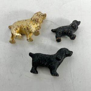 May include: Three small dog figurines. One is gold, and the other two are black.