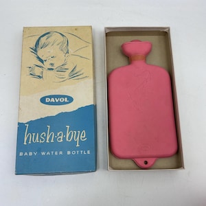May include: A pink rubber hot water bottle in its original box. The box is blue and white and says "Hush-a-bye Baby Water Bottle" and "Davol" on it.