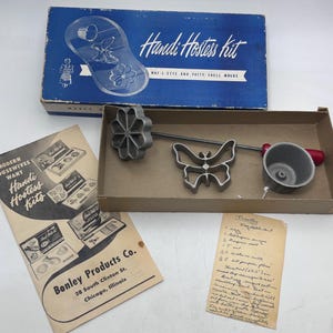 May include: Vintage Handi Hostess Kit with waffle and patty shell molds. The kit includes a blue box with the text "Handi Hostess kit", a flower-shaped mold, a butterfly-shaped mold, and a small cup with a red handle. Also included is a recipe.