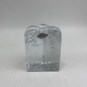 Puede incluir: Un portavelas de vidrio transparente con una superficie texturizada. El portavelas tiene una base cuadrada y un cuerpo rectangular. La etiqueta en el portavelas dice "Blenko Handcraft Made in USA".