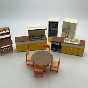 May include: A collection of miniature dollhouse kitchen furniture, including a stove, refrigerator, sink, and dining table with chairs. The furniture features a yellow and brown color scheme, with a wooden finish. The set is designed for play and display.