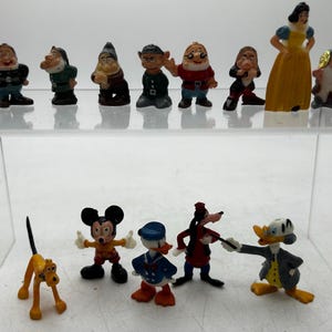May include: A collection of Disney character figurines, including Snow White, the Seven Dwarfs, Mickey Mouse, Donald Duck, Goofy, and Pluto. The figurines are brightly coloured and made of plastic.