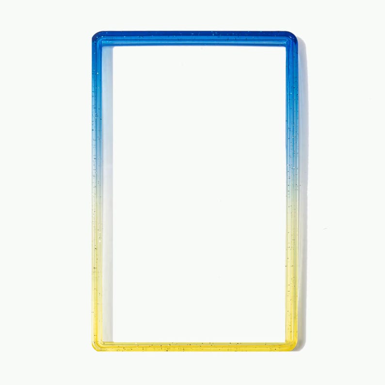 May include: A rectangular frame with a smooth, glossy finish featuring a vertical color gradient that transitions from a deep blue at the top to a bright yellow at the bottom. The frame has a hollow center and contains subtle glitter particles.
