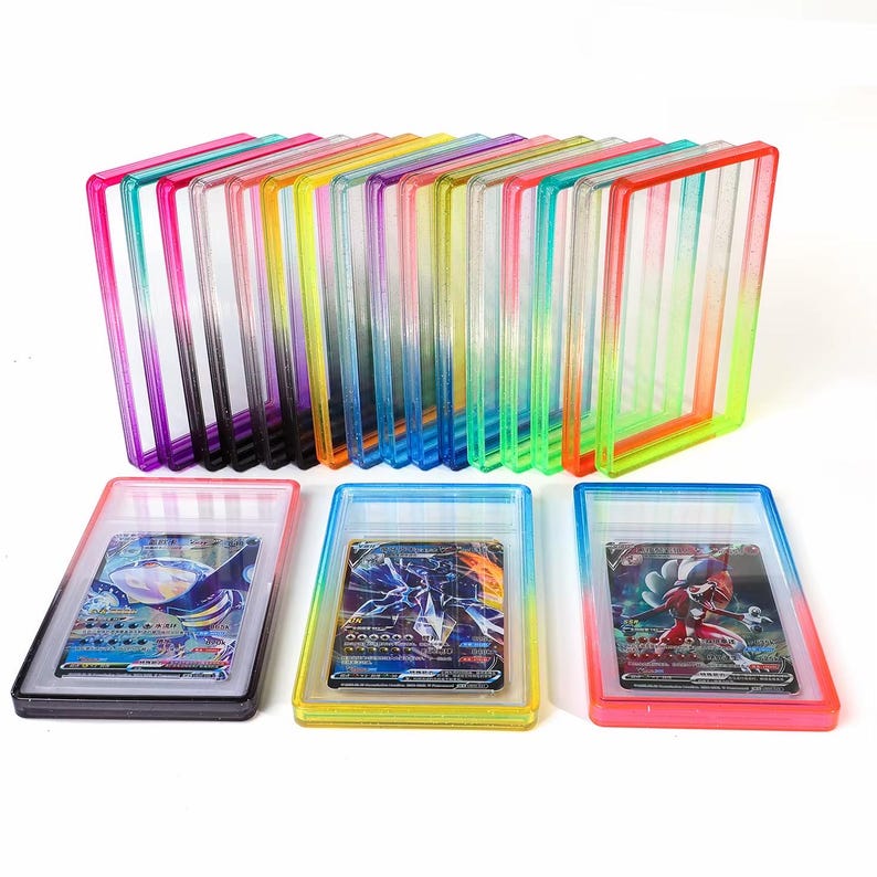 May include: A collection of rectangular, transparent plastic card holders in various neon colors, including pink, purple, yellow, blue, green, and orange. Three holders contain illustrated trading cards, while others are empty and stacked upright.