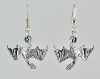 Peut inclure: Une paire de boucles d'oreilles en argent en forme de dragon avec un design détaillé. Les dragons sont en position de vol, les ailes déployées.