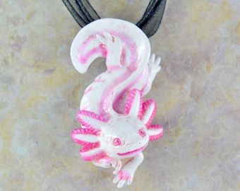 May include: A pink and white axolotl pendant necklace. The axolotl is a type of salamander with feathery gills. The pendant is made of polymer clay and is about 2 inches tall.