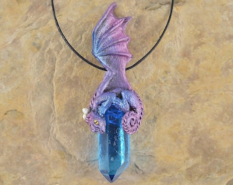 May include: A purple and blue dragon pendant with a blue crystal. The dragon is curled around the crystal and has a gold eye. The pendant is hanging from a black cord.