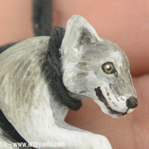 May include: A hand-painted wooden wolf figurine with a gray and white coat, black eyes, and a black rope around its neck.