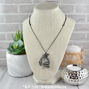 May include: A silver dragon pendant necklace on a black cord. The dragon is in a curled position with its wings spread out. The necklace is displayed on a white mannequin.