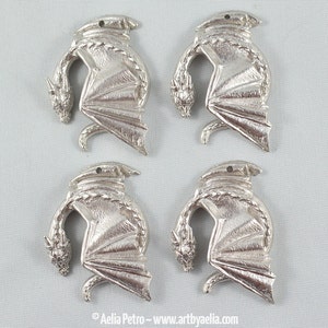 May include: Four silver-colored metal dragon charms, each with a curled tail and outstretched wings. The charms are detailed with textured scales and a raised design.