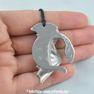 May include: Silver pendant featuring a detailed dragon design with wings outstretched. The pendant is attached to a black cord.
