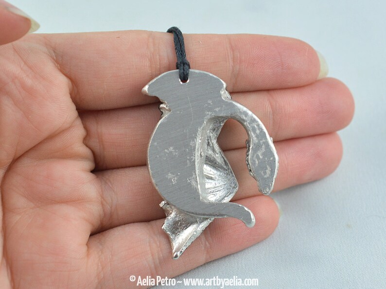 May include: Silver pendant featuring a detailed dragon design with wings outstretched. The pendant is attached to a black cord.