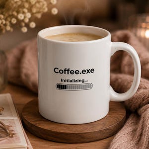 May include: A white ceramic mug filled with a hot beverage, featuring the black printed text Coffee.exe, the word Initialising, and a loading progress bar graphic on the front. The mug has a smooth finish and a curved handle on the right side.