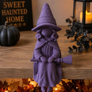 May include: A purple figurine of a witch wearing a pointed hat and a cloak, sitting with legs dangling. The witch holds a small broomstick horizontally across the lap. The figure has a smooth, matte finish and no facial features.
