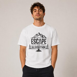 May include: A white short-sleeved t-shirt featuring a black graphic print on the chest. The design includes a mountain range, pine trees, a tent, and the text "ESCAPE THE ALGORITHM" centered in a bold, sans-serif font with horizontal lines.