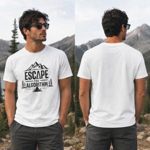 May include: A white short-sleeved t-shirt featuring a black graphic on the front. The design includes a mountain range, pine trees, a small tent, and the text "ESCAPE THE ALGORITHM" in a bold, sans-serif font. The back of the t-shirt is plain white.