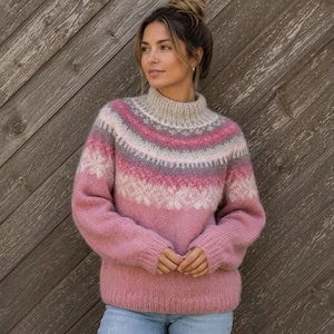 May include: A long-sleeved knit jumper featuring a high mock neck and a fair isle pattern across the chest and shoulders. The jumper displays a gradient of colours including cream, light pink, dark pink, and grey, with white snowflake motifs.