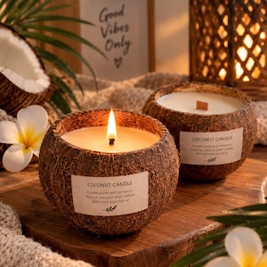 Może przedstawiać: Dwie świece w łupinach kokosa z białym woskiem i drewnianymi knotami. Każda świeca posiada prostokątną etykietę z napisem COCONUT CANDLE, Create warm and romantic, Natural coconut shell candle, With pure essential oil oraz ikoną liścia.