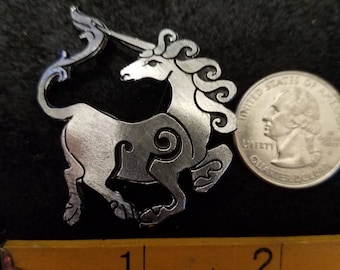 May include: A silver-colored metal unicorn pendant with intricate details. The pendant is approximately 1 inch in size and is shown next to a US quarter for scale.