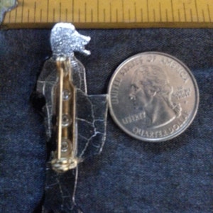 Puede incluir: Un broche negro y plateado con forma de mujer. El broche es aproximadamente del tama&ntilde;o de una moneda de 25 centavos.