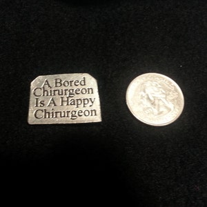 May include: A silver charm with the inscription "A Bored Surgeon Is A Happy Surgeon".