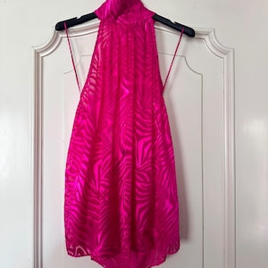 Può includere: Un top all'americana color rosa acceso vibrante caratterizzato da un sottile motivo a righe zebrate tono su tono su tutto il tessuto. Il capo presenta uno scollo alto, sottili spalline che partono dai lati e un design senza maniche.