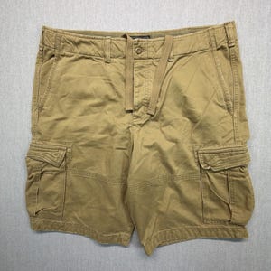 Puede incluir: Pantalones cortos tipo cargo de color tostado con cierre de botón, cremallera y cordón integrado en la cintura. Los pantalones incluyen dos grandes bolsillos laterales tipo cargo con solapa, dos bolsillos delanteros y trabillas.