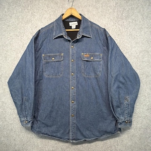 May include: A blue denim long-sleeve shirt with a black interior lining, a pointed collar, and a front button closure. The shirt features two chest pockets with button flaps, metal buttons, and a Carhartt brand label on the inner neck.