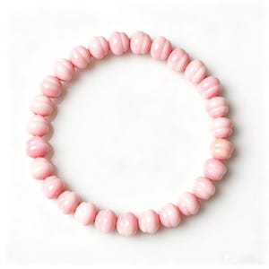 May include: A circular bracelet composed of numerous light pink beads. Each bead features a distinct ribbed or grooved texture, creating a uniform pattern around the entire circumference of the jewellery piece. The beads are arranged in a continuous loop.
