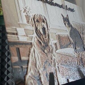 K&ouml;nnte beinhalten: Eine rechteckige 3D-gedruckte Platte mit einem strukturierten Reliefbild eines Golden Retrievers und einer schwarz-wei&szlig;en Katze, die zusammen auf einem Sofa sitzen. Der Text "Unconditional Love" ist in Schreibschrift oben auf der Platte eingepr&auml;gt.