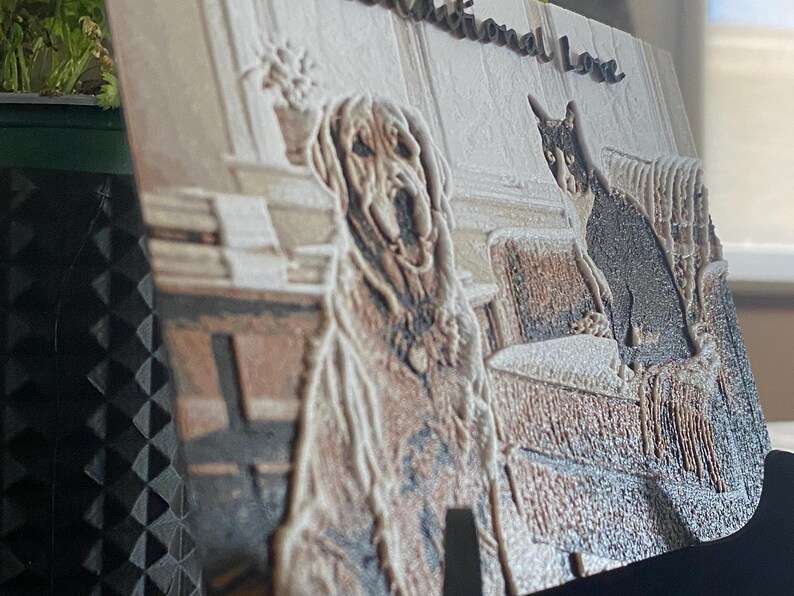 K&ouml;nnte beinhalten: Eine rechteckige 3D-gedruckte Platte mit einem strukturierten Reliefbild eines Golden Retrievers und einer schwarz-wei&szlig;en Katze, die zusammen auf einem Sofa sitzen. Der Text "Unconditional Love" ist in Schreibschrift oben auf der Platte eingepr&auml;gt.