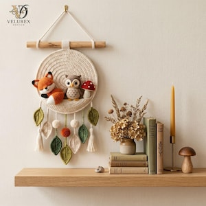 May include: A circular cream-coloured crochet wall hanging featuring a fox, an owl, and a mushroom. The piece is suspended from a wooden dowel and decorated with dangling crochet leaves, pom-poms, and tassels. The text VELUREX DESIGN is visible.