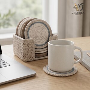 May include: A set of round, crocheted coasters in beige and light blue, stored in a matching square crocheted holder. One coaster sits under a plain white ceramic mug. The coasters feature a spiral pattern with a light blue ring accent.