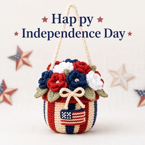 May include: A crocheted basket with red, white, and blue vertical stripes, featuring a small American flag patch and a cream-colored bow. The basket is filled with crocheted red, white, and blue flowers and green leaves, with the text Happy Independence Day.