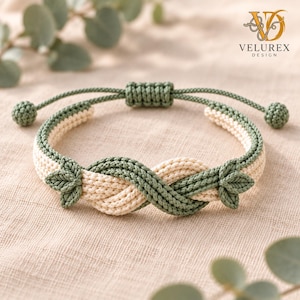Può includere: Un bracciale in macramè caratterizzato da un design intrecciato in corda color verde salvia e crema. Il bracciale presenta decorazioni a forma di foglia sui lati e una chiusura a nodo scorsoio regolabile con due piccole estremità sferiche.