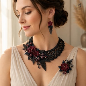 Puede incluir: Un collar de encaje negro con detalles florales en rojo oscuro y motivos de hojas de helecho, pendientes a juego con una flor roja y hoja de helecho negra, y un broche floral con hojas de helecho negras y bayas rojas.