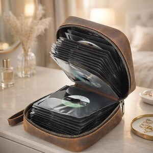 May include: A brown leather storage case with a zipper closure, designed to hold multiple discs. The case is open, revealing several clear plastic sleeves inside, each containing a disc. A small leather strap is attached to the side of the case.