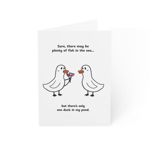 May include: A white greeting card featuring two cartoon ducks with orange beaks. One duck holds a small bouquet of flowers. The text reads: Sure, there may be plenty of fish in the sea... but there's only one duck in my pond.