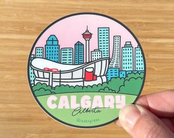 May include: A round sticker featuring a Calgary, Alberta, Canada skyline. The design includes a stadium, skyscrapers, and the Calgary Tower, set against a pink sky and green foreground. The text "CALGARY Alberta" is displayed.