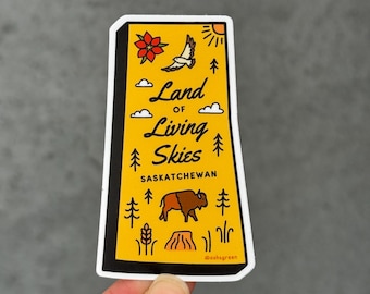 Puede incluir: Una pegatina rectangular con fondo amarillo y borde negro. La pegatina presenta el texto "Land of Living Skies Saskatchewan" con ilustraciones de una flor, un pájaro, el sol, árboles, nubes, un bisonte y una espiga de trigo.