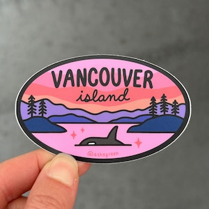 May include: An oval sticker with a pink and purple sunset design, featuring the text "Vancouver Island" and an orca whale. The sticker also includes trees, water, and stars. The artist's name, "@ashsgreen", is at the bottom.