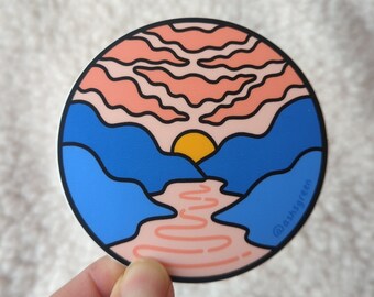 May include: A circular sticker featuring a stylized landscape with a yellow sun setting behind blue mountains. Above the sun are peach-colored wavy clouds, and below, a peach-colored river flows through the mountains. The text @ashsgreen is visible.