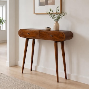 May include: A medium-brown wooden console table featuring a rounded rectangular top with two drawers, each equipped with a small dark metal knob. The table is supported by four tapered, angled legs and has a smooth, polished wood grain finish.